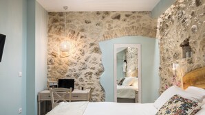 Een slaapkamer met een stenen muur, een bed met wit beddengoed, een houten hoofdbord en een spiegel.