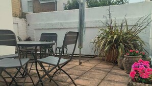A patio with a table and chairs, potted plants, and a white wall in the background. - Stunning 1-bed Apartment in Southsea (Portsmouth)