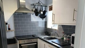 A compact kitchen with white cabinets, a black countertop, and a tiled backsplash. - Stunning 1-bed Apartment in Southsea (Portsmouth)