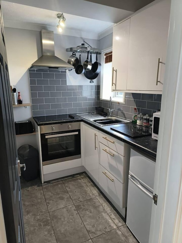 Compact kitchen with oven, sink, and range hood, featuring white cabinetry and a black countertop.