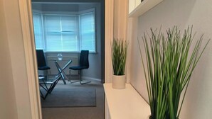 A hallway with a white console table, a potted plant, and a view into a room with a dining table and chairs. - Stunning 1-bed Apartment in Southsea (Portsmouth)