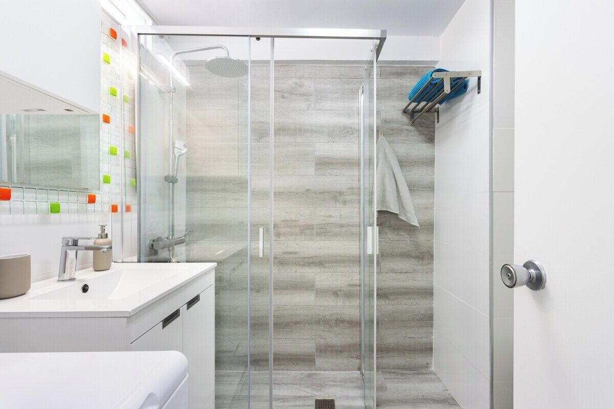 Un baño moderno con cabina de ducha de vidrio, lavamanos blanco y espejo con notas adhesivas de colores.