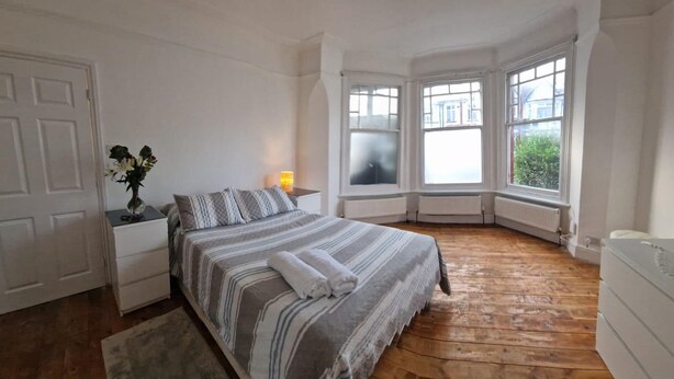 Un dormitorio con cama, mesita de noche, lámpara y vistas al exterior a través de amplias ventanas.