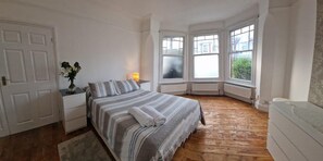 A bedroom with a bed, bedside table, lamp, and a view of the outside through large windows. - 1 Bed Flat - Sleeps 2 - Pets - Parking - Wifi (London)