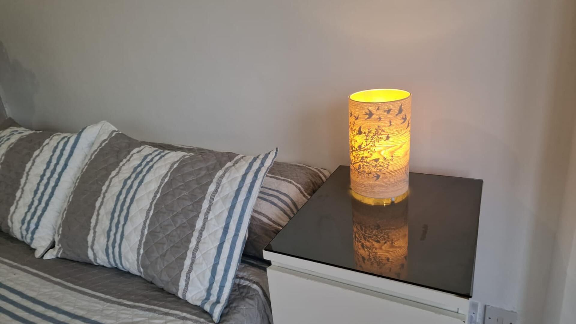 Ein Bett mit gestreiften Kissen und einem Nachttisch mit Lampe.
