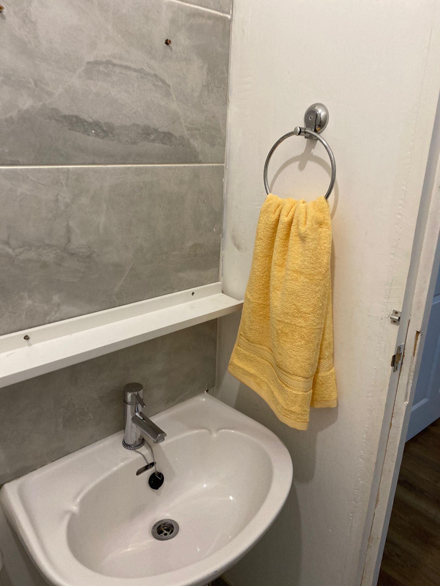 A bathroom with a white sink, a mirror, and a towel rack with a yellow towel.