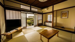 A traditional Japanese-style room with tatami flooring, a low wooden table, a television, and sliding doors leading to a garden. - Yamamo Onomichi (Onomichi)