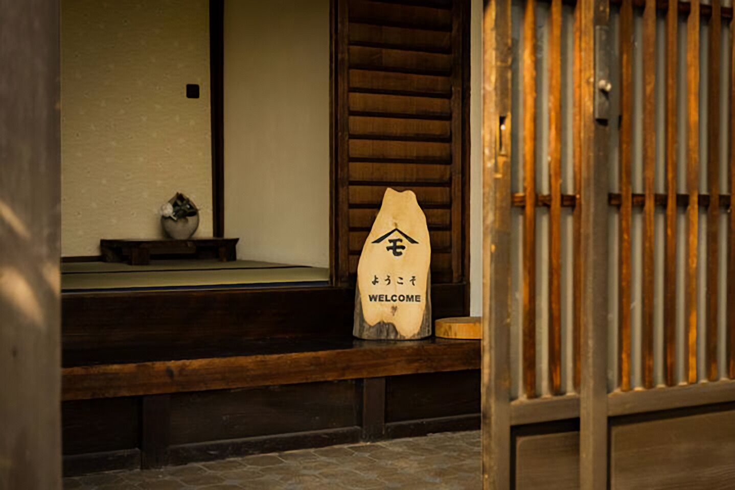 A wooden bench with a welcome sign in front of a traditional Japanese sliding door.