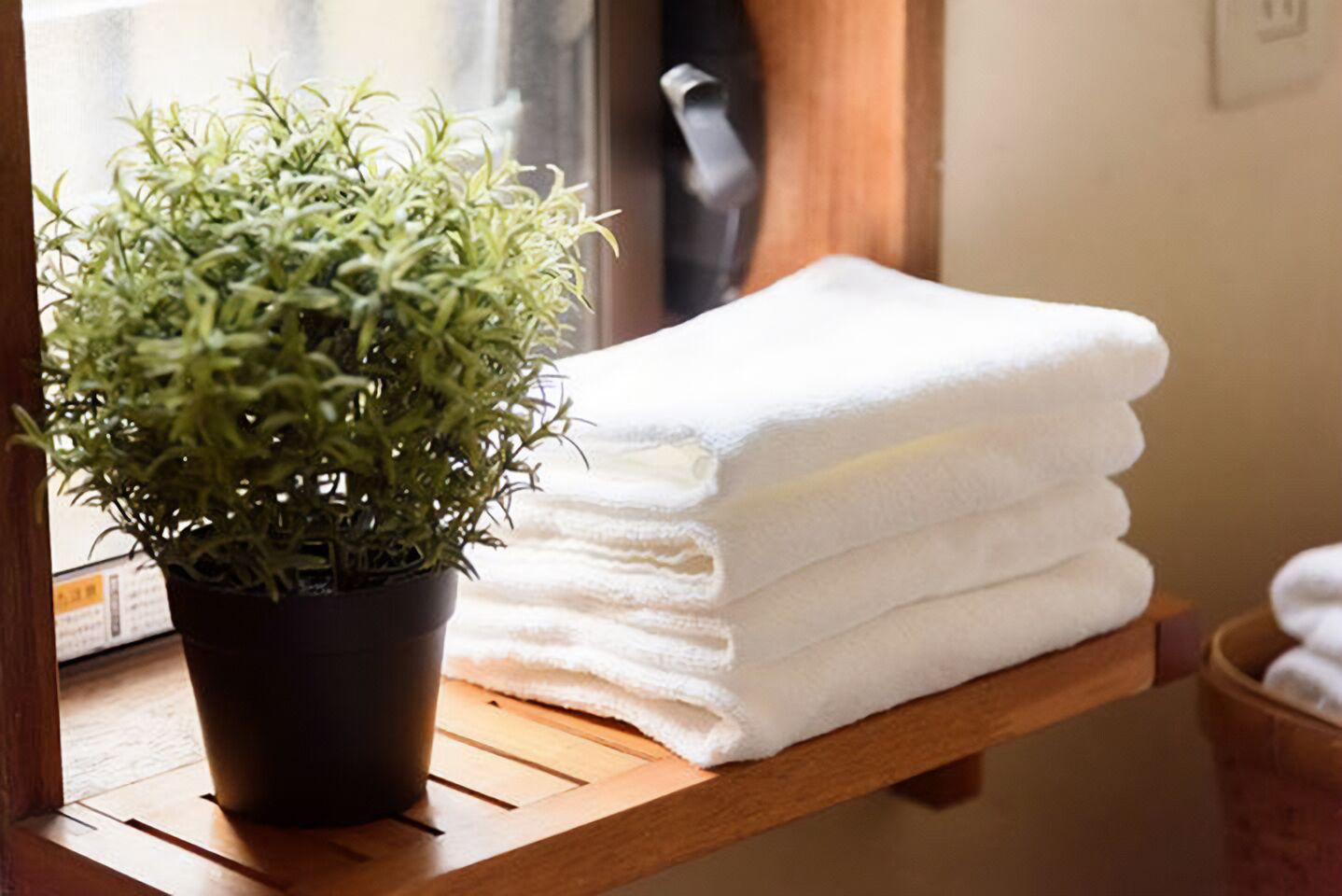 A potted plant next to a stack of white towels on a wooden shelf.