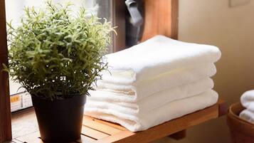 A potted plant next to a stack of white towels on a wooden shelf.