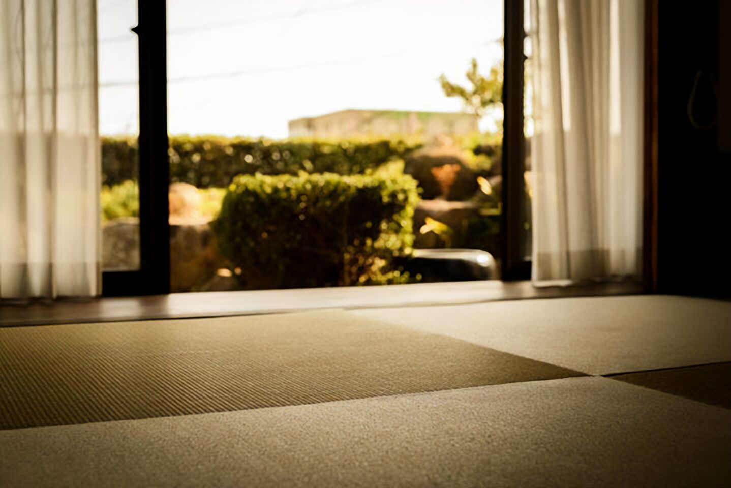 Habitació amb estera de tatami i vistes a un jardí a través d'una finestra amb cortines blanques.