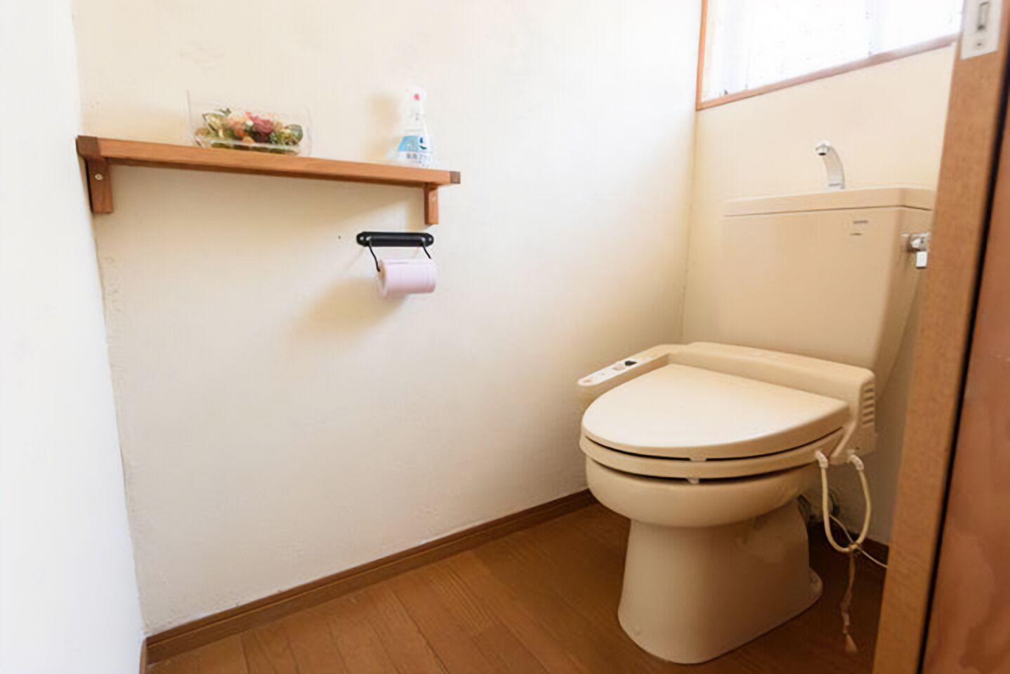Une petite salle de bain compacte, comprenant des toilettes, une étagère avec un porte-rouleau de papier toilette et une petite fenêtre.