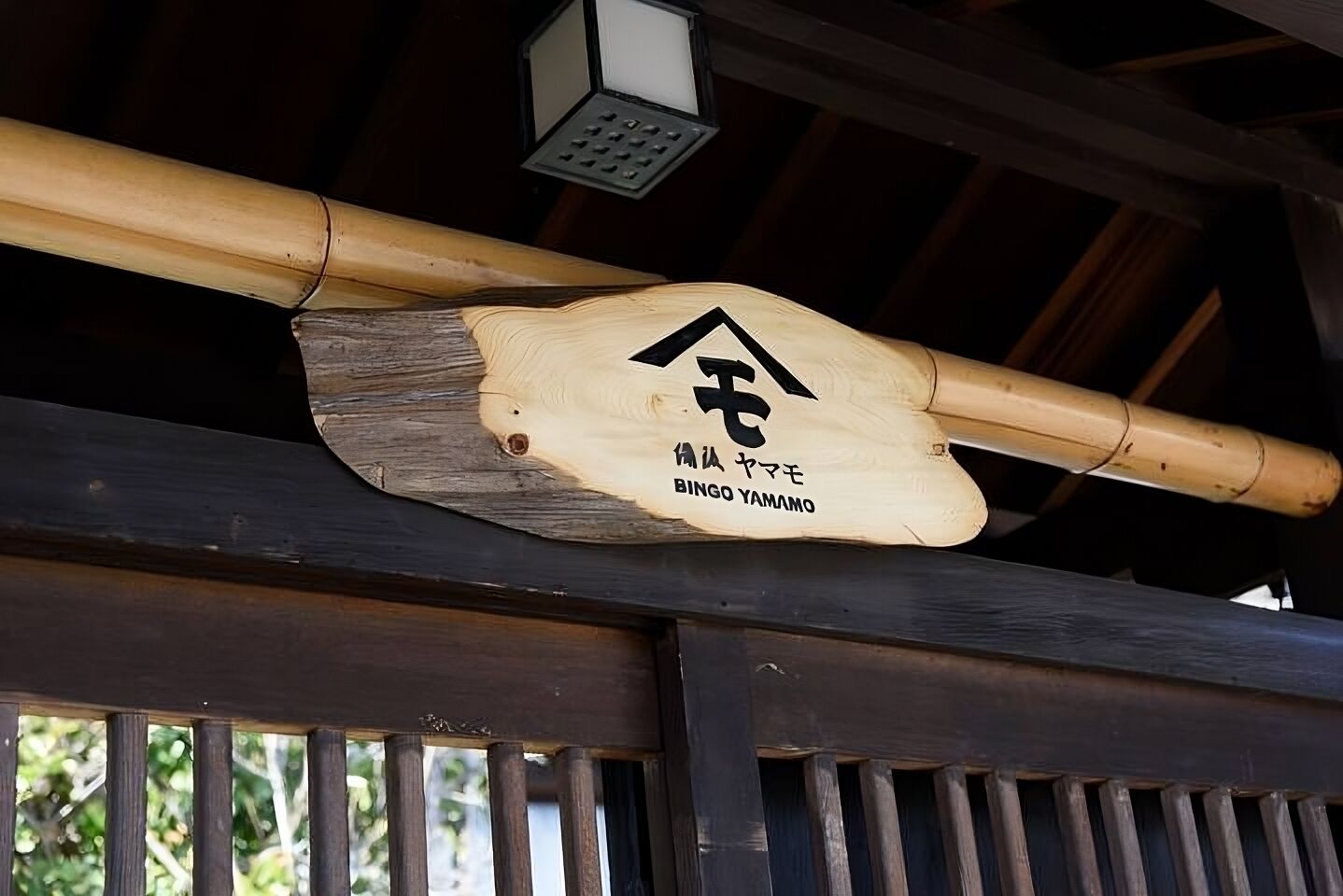 Une enseigne en bois, ornée de caractères japonais et portant l’inscription « BINGO YAMAMOTO », est suspendue à une structure en bambou.