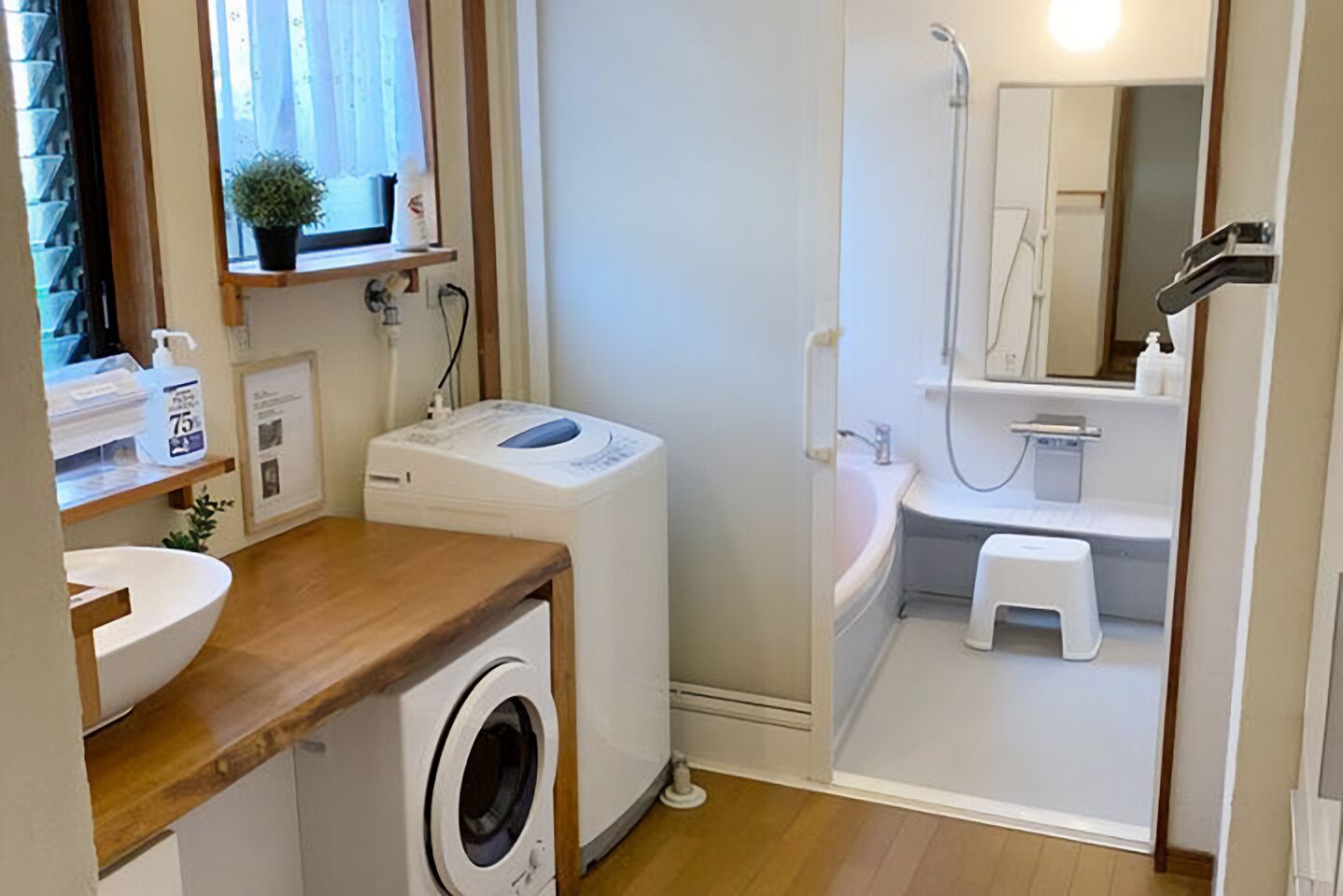 A compact bathroom with a washing machine, a sink, a shower, and a small stool.