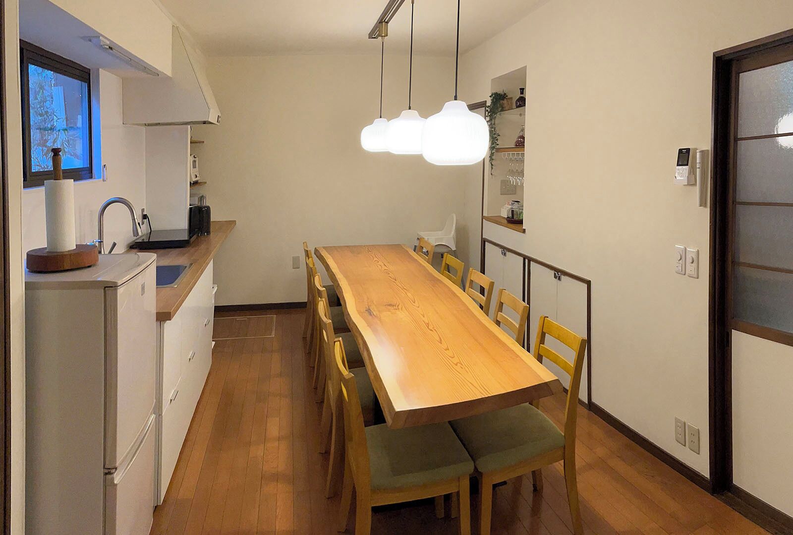 Une cuisine compacte avec une table et des chaises en bois, un four encastré et une fenêtre équipée de stores.