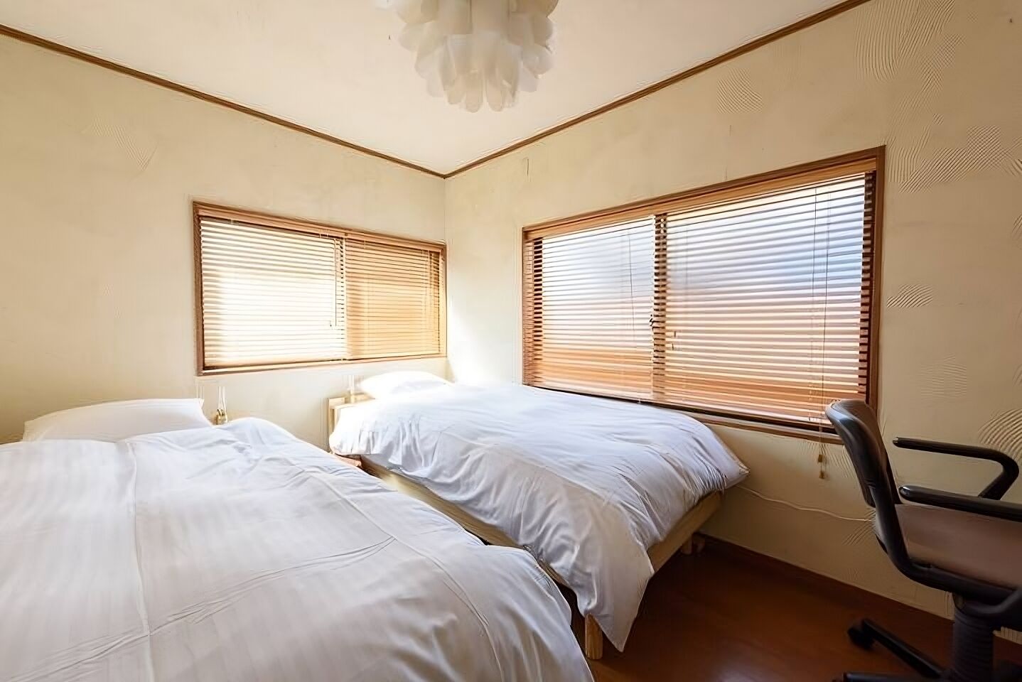 A bedroom with two beds, wooden blinds, a desk, and a chair.