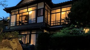 A traditional Japanese-style building with multiple windows and a balcony, surrounded by greenery. - Yamamo Onomichi (Onomichi)