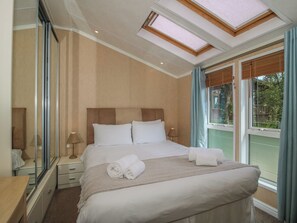 A hotel room with a large bed, a bedside table, a mirror, and a skylight. - Daisy (Leominster)