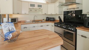 A modern kitchen with white cabinetry, a wooden countertop, a stainless steel stove, and a hanging pot rack.