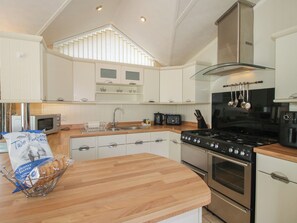 A modern kitchen with white cabinetry, a wooden countertop, a stainless steel stove, and a hanging pot rack. - Daisy (Leominster)
