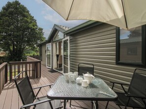Une terrasse extérieure avec une table dressée pour le thé, des chaises et un grand parasol.