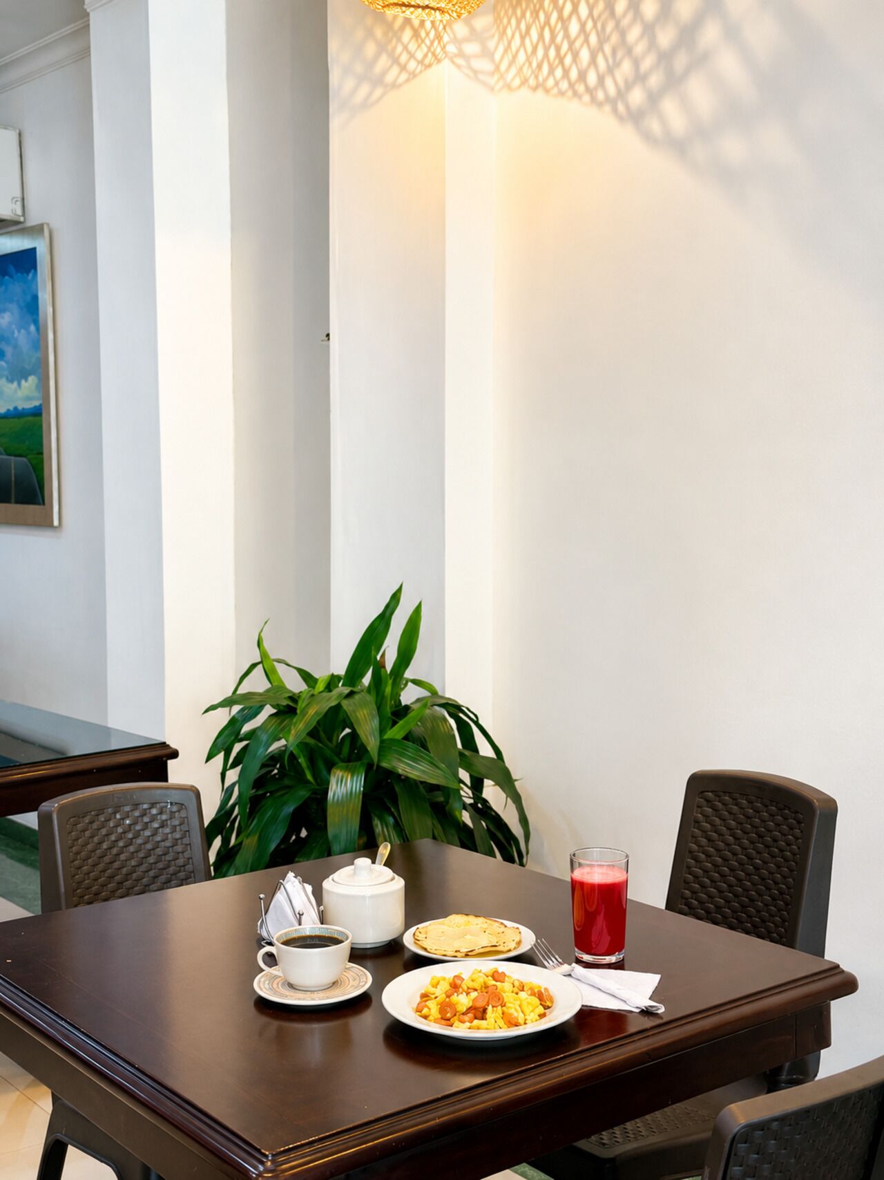 A dining table with a plant, a cup, a plate of food, and a glass of red drink.