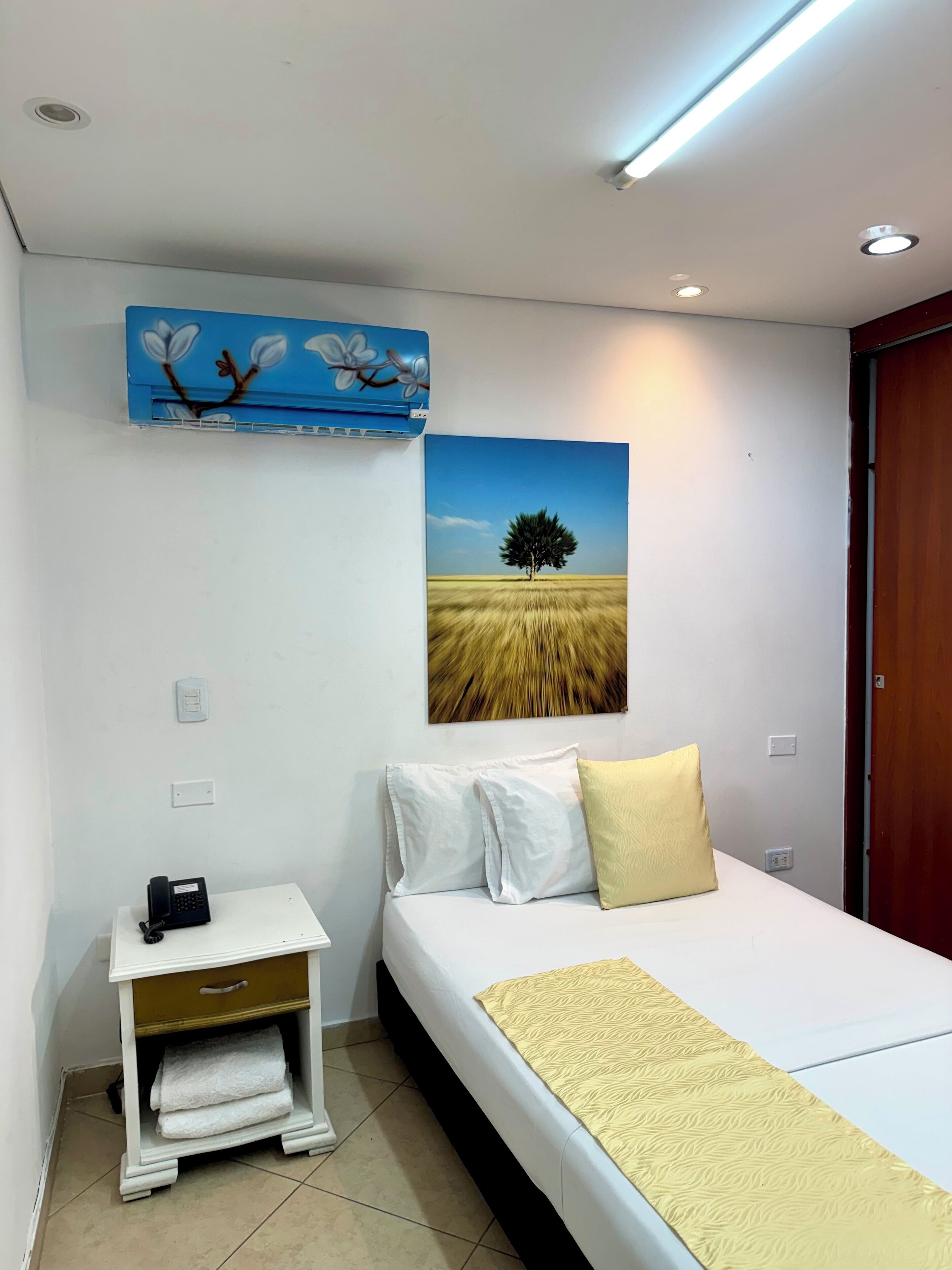 Un dormitorio con cama, mesita de noche, teléfono, un cuadro y una puerta.
