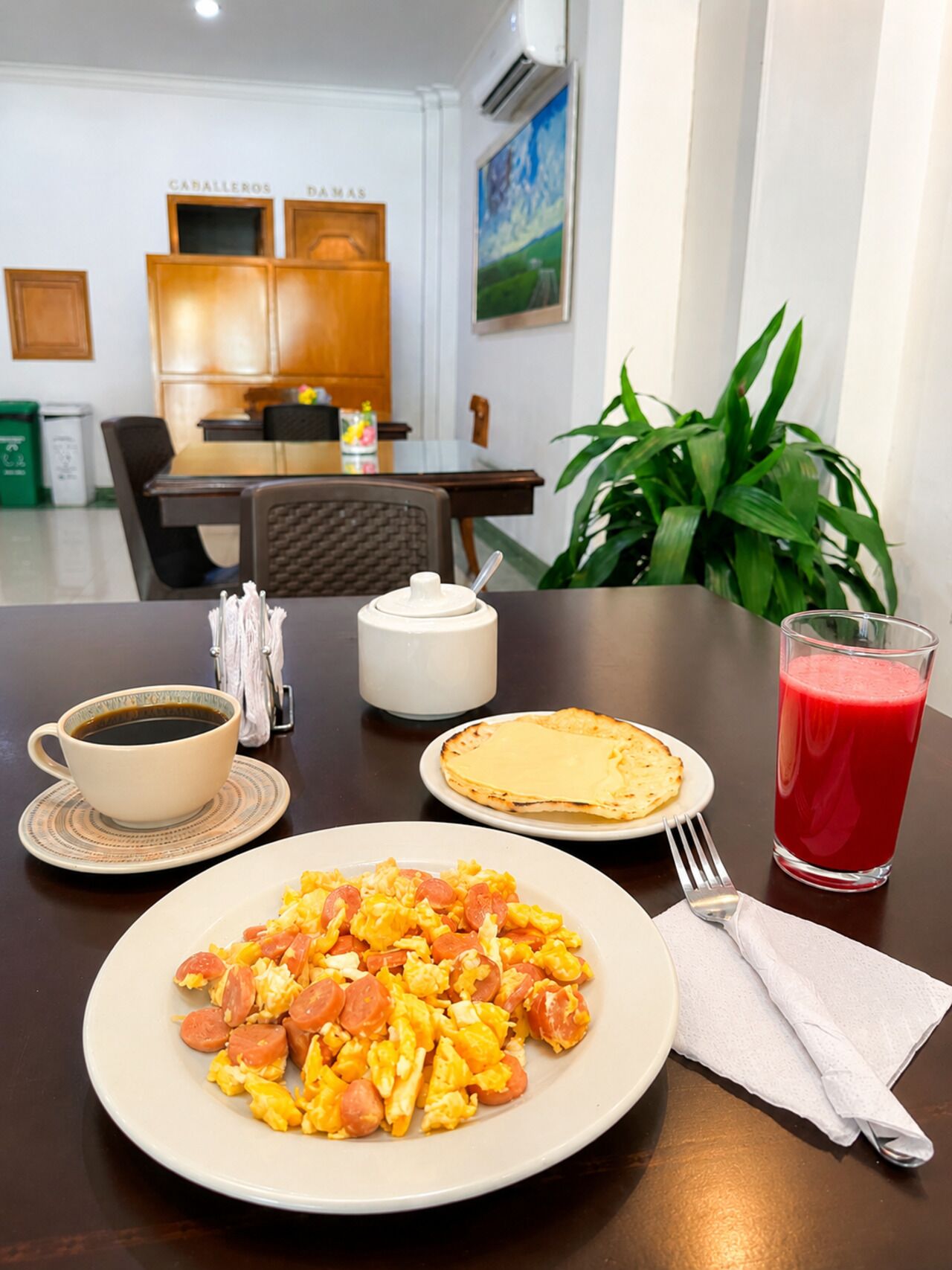 A breakfast setting with scrambled eggs, toast, coffee, and a glass of red juice on a table.