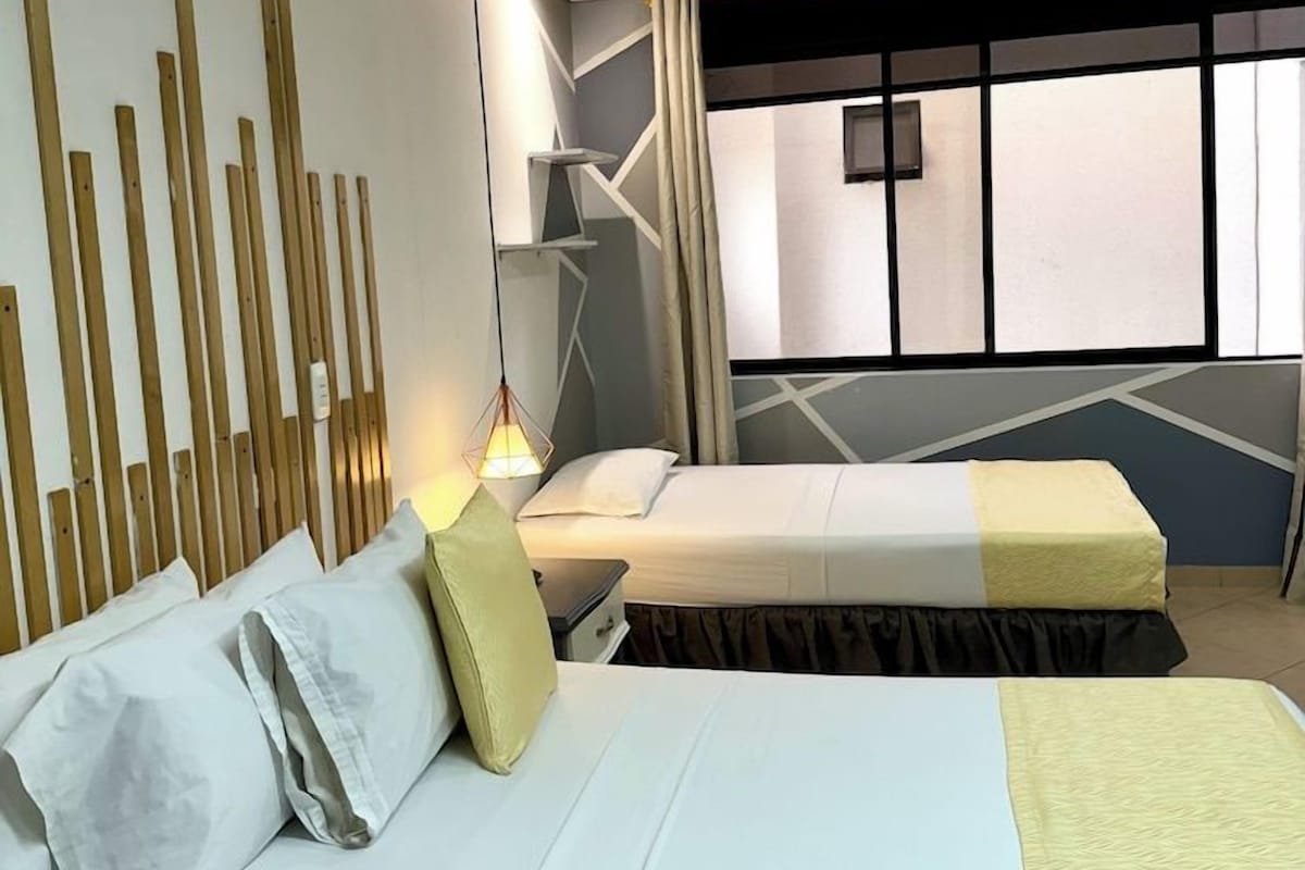 A hotel room with two beds, a modern wall design, and a large window.