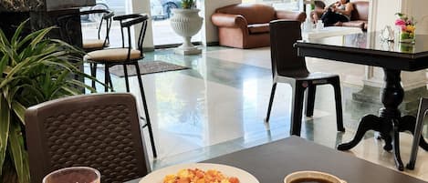 Vestíbulo de hotel con mostrador de recepción, zona de estar y una mesa de desayuno con alimentos.