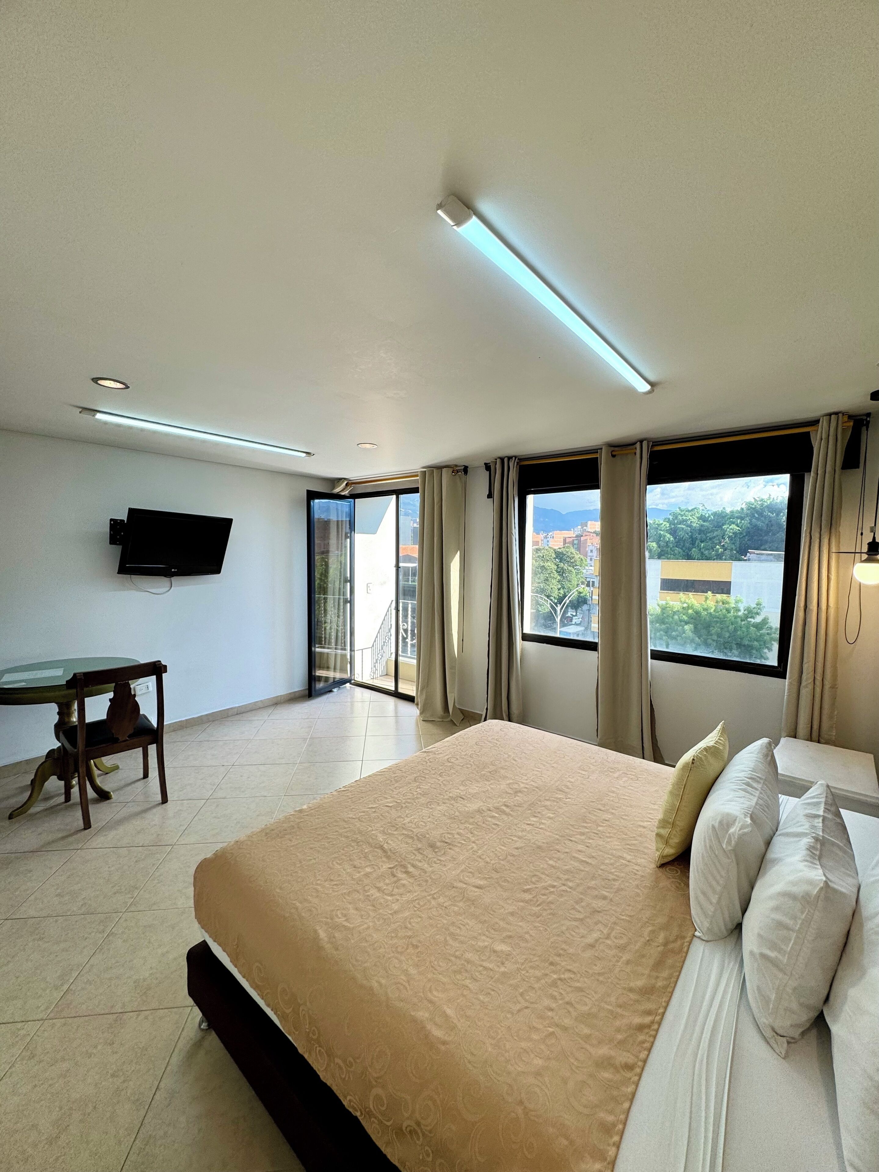 Une chambre d’hôtel dotée d’un grand lit, d’un bureau avec une chaise, d’un téléviseur à écran plat fixé au mur et d’un balcon offrant une vue sur la ville.