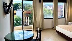 A hotel room with a bed, a table with a chair, a TV mounted on the wall, and large windows with curtains. - Hotel Prince Plaza - Laureles (Medellín)