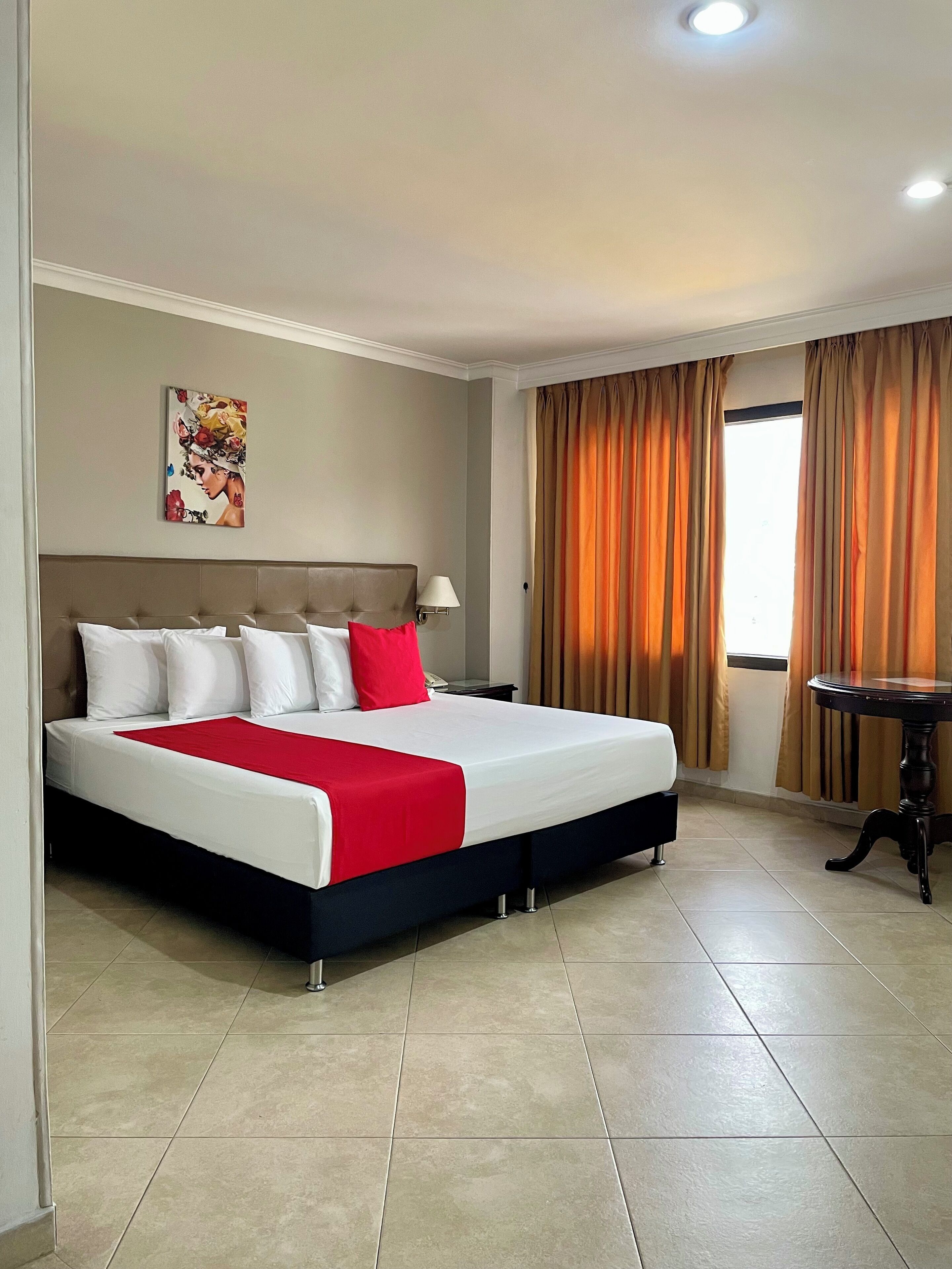 A hotel room with a large bed, a bedside table, a lamp, and a window with curtains.