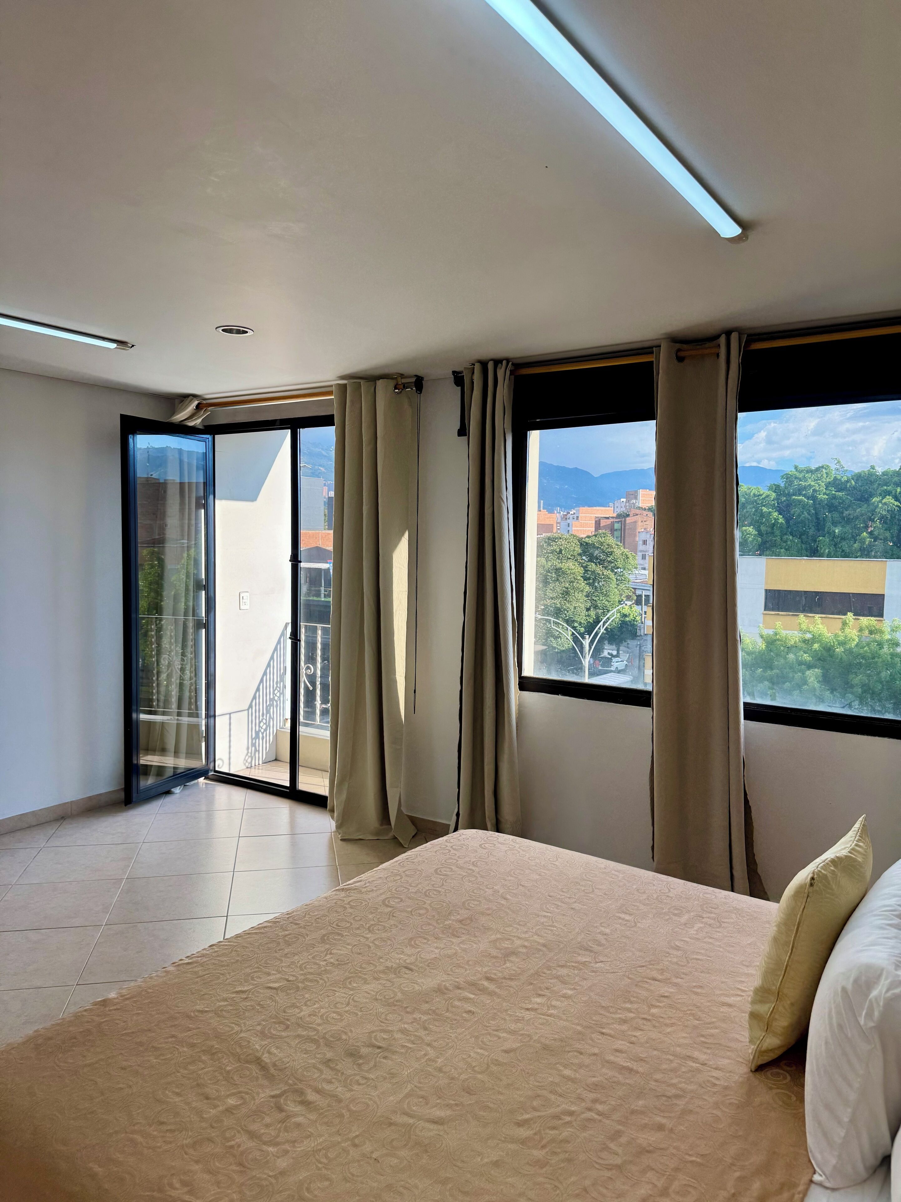 Une chambre avec un grand lit, une porte-fenêtre coulissante donnant sur un balcon et une vue sur la ville.
