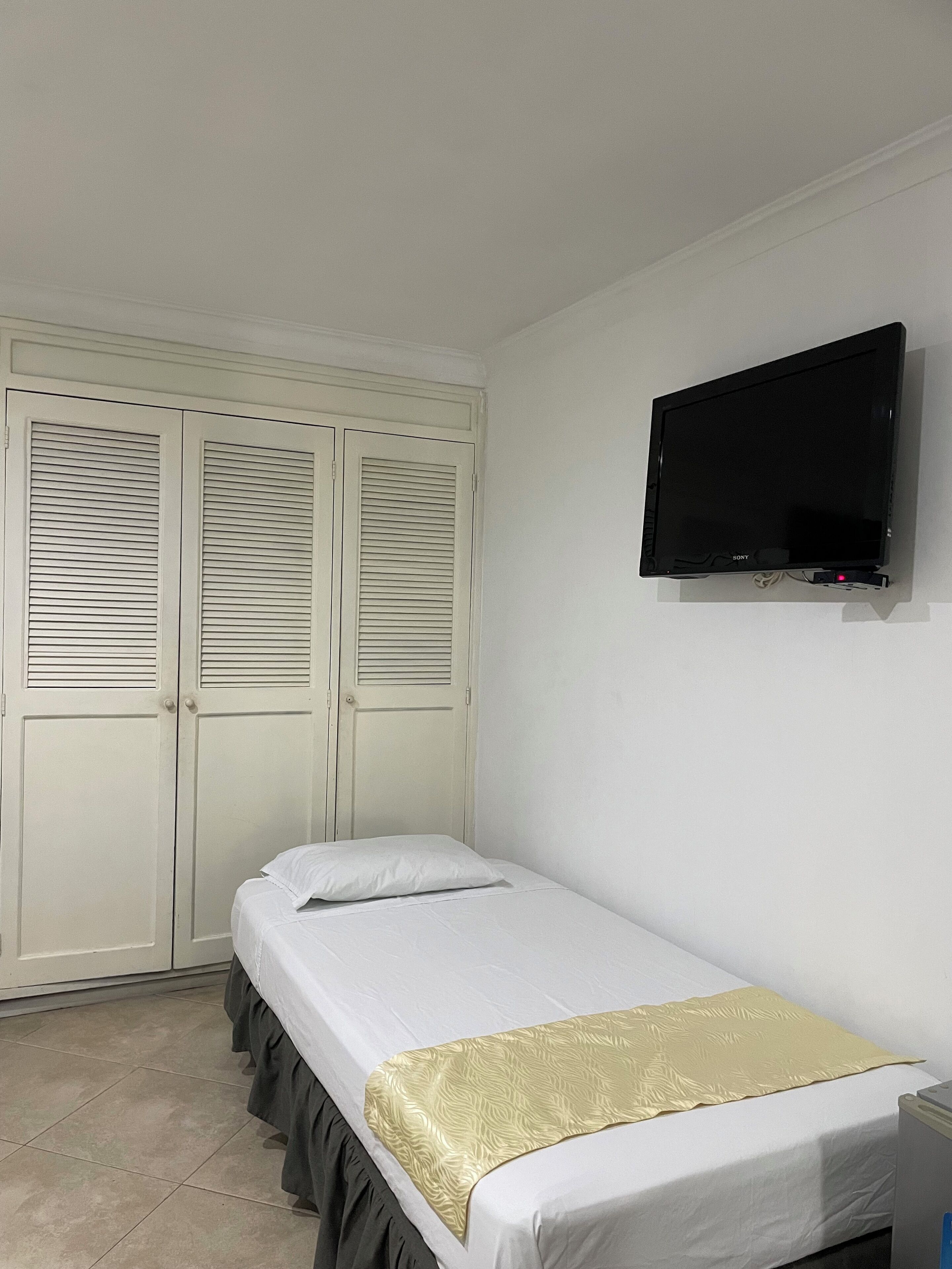 A bedroom with a bed, a TV mounted on the wall, and a wardrobe with louvered doors.