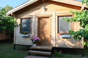 Una cabaña de madera con puerta principal, dos ventanas y un pequeño porche con escalones.