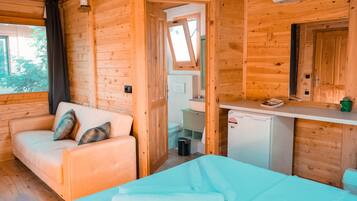 A wooden cabin room with a sofa, a small table, a bed, a kitchenette, and a window.