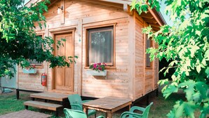 Une cabane en bois avec une porte d’entrée, des fenêtres et un petit porche équipé d’une table et de chaises.