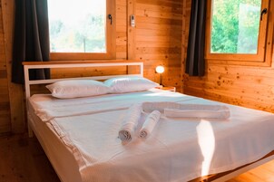 Una habitación de cabaña de madera con una cama, una mesita de noche y una ventana.