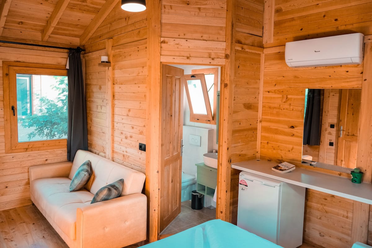 Ein Holzblockhaus-Innenraum mit einer Couch, einer kleinen Küchenzeile und einem durch eine offene Tür einsehbaren Badezimmer.