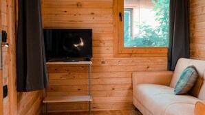 Une pièce de cabane en bois avec un téléviseur posé sur un meuble, un canapé et une fenêtre avec des rideaux.