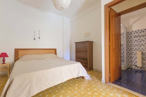 Ein Schlafzimmer mit Bett, Nachttisch mit Lampe, Kommode und Musterfliesen.