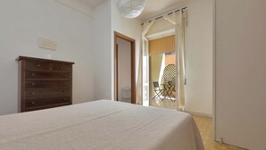 Un dormitorio con cama, cómoda de madera y vista a un espacio exterior con una silla y una mesa.