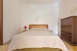 Un dormitorio con cama, mesita de noche, cómoda y lámpara de pared.