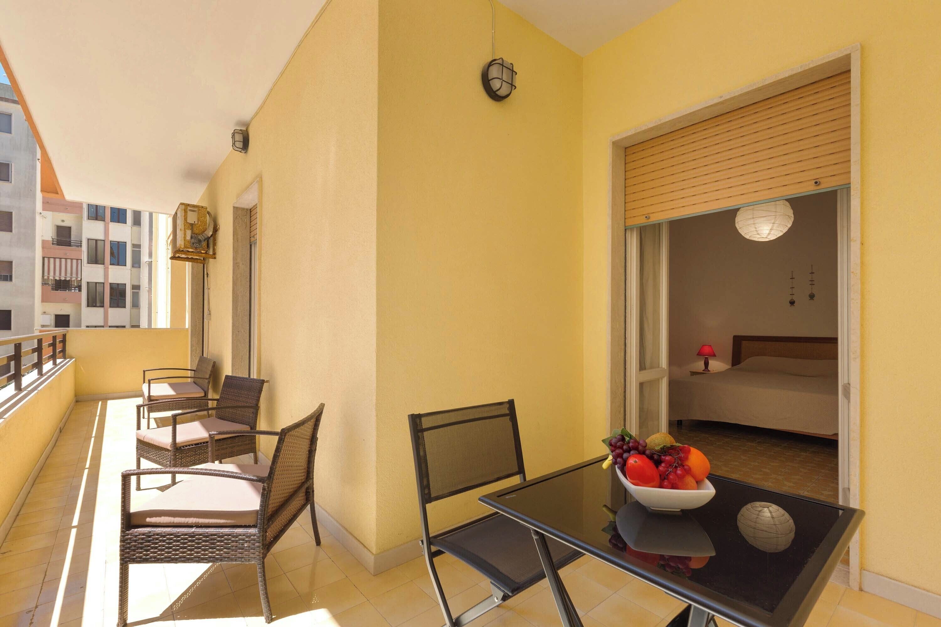 A balcony with wicker chairs, a glass table with a fruit bowl, and a view of a bedroom with a bed and a nightstand.