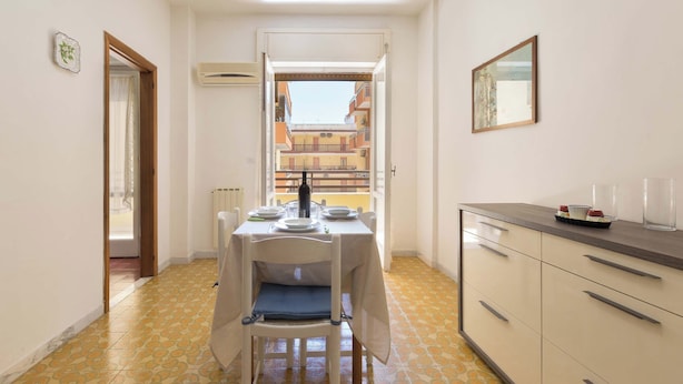 Un pasillo estrecho con una mesa de comedor dispuesta para dos personas, un radiador y vistas de un edificio a través de una puerta abierta.