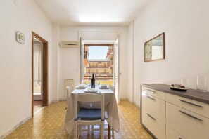 Un pasillo estrecho con una mesa de comedor dispuesta para dos personas, un radiador y vistas de un edificio a través de una puerta abierta.