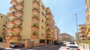 Un edificio residencial de varios pisos con balcones, entrada protegida y automóviles estacionados.