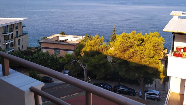 Un balcó amb vista al mar, edificis i cotxes aparcats.