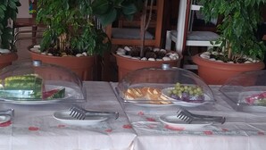 Taula de buffet amb plats de menjar coberts, envoltada d'arbres en testos.